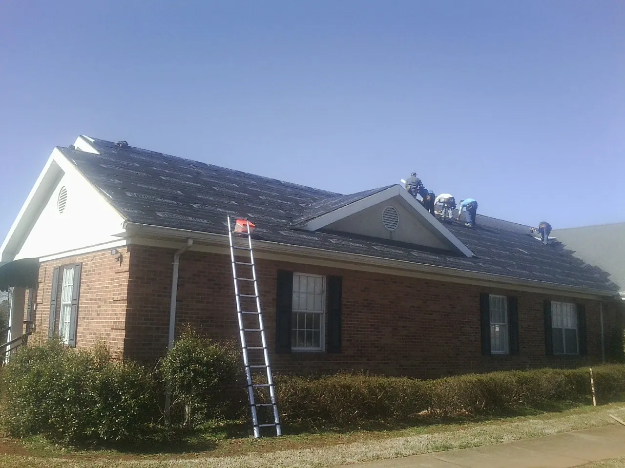 Crew tearing shingles off a brick ranch roof with a ladder set — Emergency Roof Repair work by our crew in Hickory Hills
