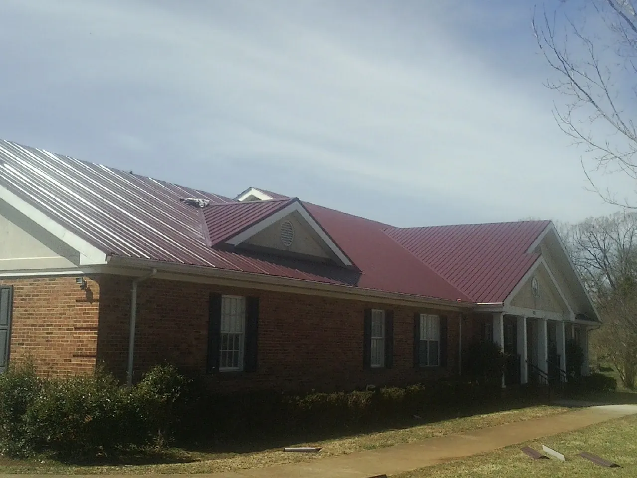 Red metal roof with gabled entries on a long brick building, from a Hail Damage Roof Repair job in Hickory Hills