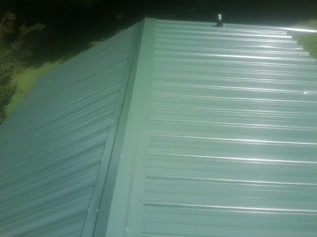 New green metal panels meeting at the ridge of a roof — Flat Roof Repair work by our crew in Hickory Hills