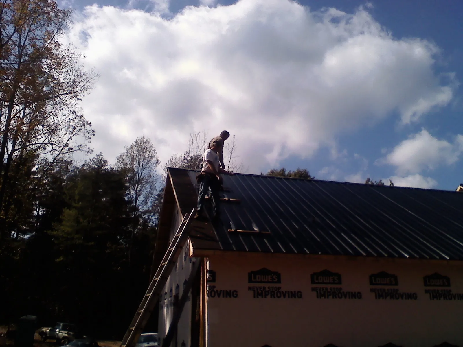 Roofer fastening dark metal panels high against a cloudy sky, from a Roof Inspection job in Hickory Hills