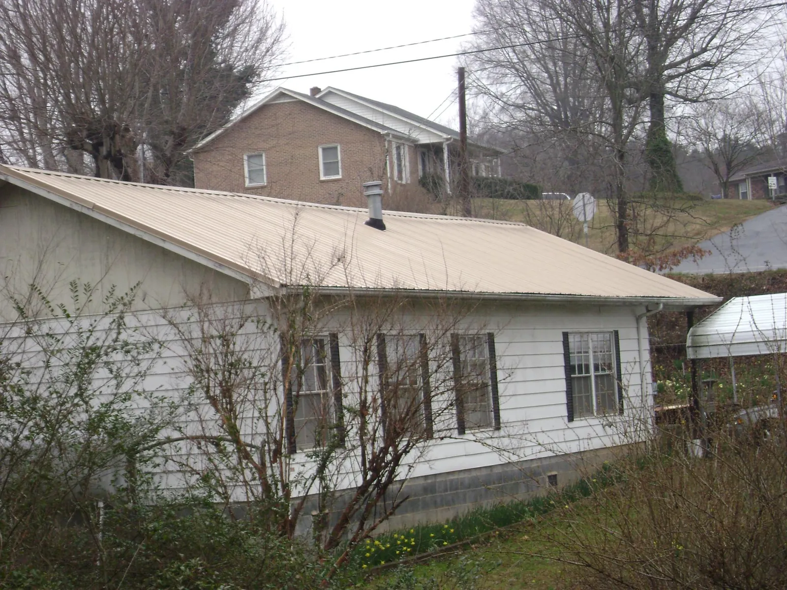 Tan metal roof on a white sided house set into a hillside — Commercial Roofing by Roofing Brothers in Hickory Hills