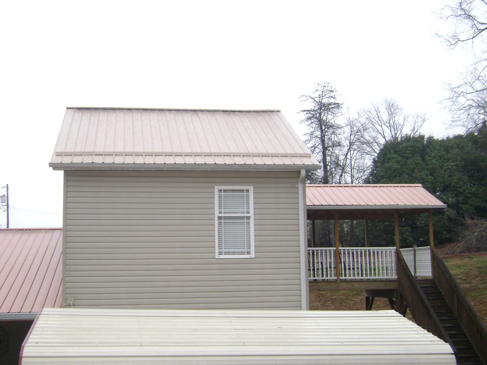 Tan metal roofs on a two story addition and attached porch, from a Roof Replacement job in Hickory Hills